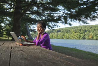 African American businesswoman sitting at picnic bench talking on cell phone