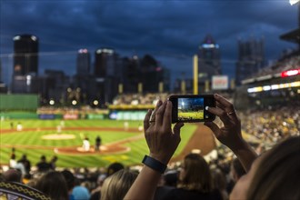 Hands of woman photographing baseball game with cell phone