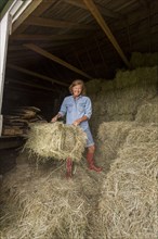 Older Caucasian woman hauling hay bales in barn
