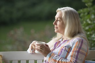 Older Caucasian woman drinking cup of coffee on porch swing