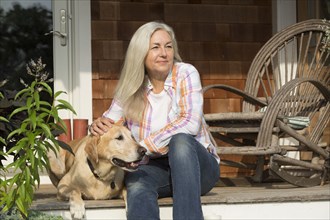 Older Caucasian woman petting dog on front porch