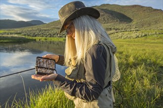 Caucasian woman examining fishing tackle near remote lake