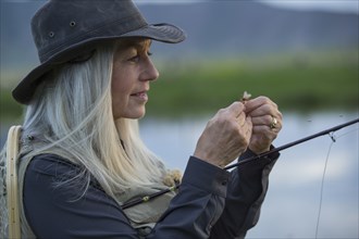 Caucasian woman tying fishing line in remote lake