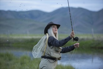 Caucasian woman casting fishing line in remote lake