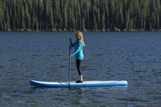 Caucasian woman standing on paddle board in river