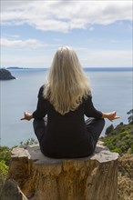 Older Caucasian woman meditating on cliff near ocean