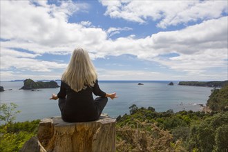 Older Caucasian woman meditating on cliff near ocean