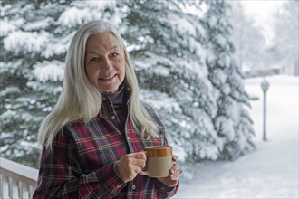 Older Caucasian woman drinking coffee on snowy patio