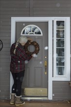 Older Caucasian woman hanging wreath on front door