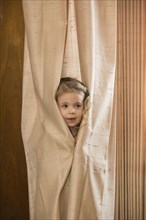 Caucasian preschooler girl hiding in curtain