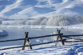 Fence and river in snowy rural landscape near river