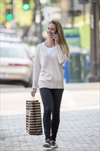 Caucasian woman carrying shopping bag using cell phone
