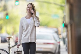 Caucasian woman carrying shopping bag using cell phone