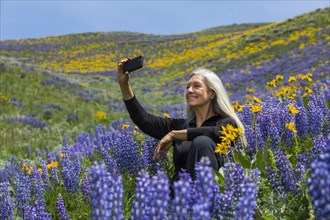 Caucasian woman posing for cell phone selfie hillside with wildflowers
