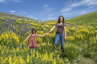 Caucasian mother and daughter standing on hillside with wildflowers