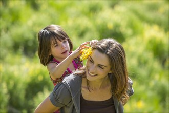 Caucasian mother carrying daughter piggyback outdoors with wildflowers