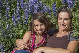 Caucasian mother and daughter laying on hillside with wildflowers
