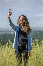Caucasian woman posing for cell phone selfie in field of tall grass