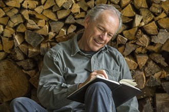 Caucasian man leaning on woodpile writing in journal