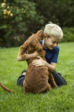 Caucasian boy hugging dog in grass