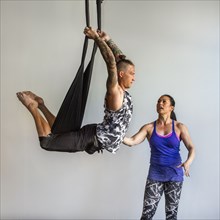 Mixed Race instructor assisting student hanging from silks