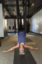 Caucasian woman performing yoga hanging from silks