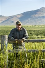 Caucasian farmer wearing gloves leaning on wooden fence
