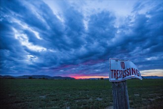 No trespassing sign under clouds at sunset
