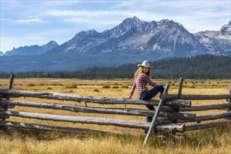 Caucasian woman sitting on wooden fence near mountain