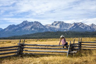 Caucasian woman sitting on wooden fence near mountain river