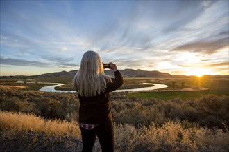 Caucasian woman photographing sunset over winding river
