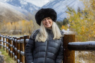 Caucasian woman wearing fur hat leaning on wooden fence in winter