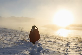 Caucasian woman shielding eyes in winter landscape at sunset