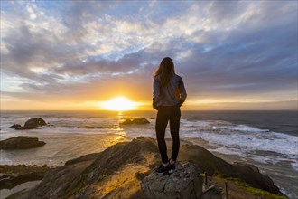 Caucasian woman standing on rock near ocean at sunset