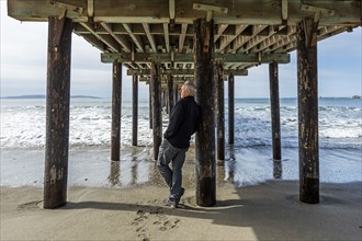 Caucasian man leaning on piling of wooden pier at beach