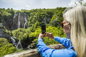 Older Caucasian woman photographing waterfalls with cell phone