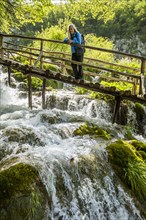 Older Caucasian woman on wooden footbridge admiring waterfall