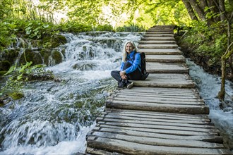 Older Caucasian woman sitting on wooden staircase over waterfalls