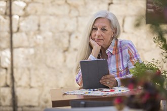 Pensive older Caucasian woman using digital tablet