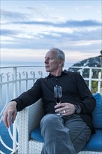 Caucasian man drinking wine on waterfront balcony
