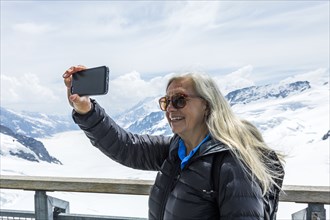 Caucasian woman posing for cell phone selfie near snowy mountains