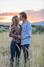 Caucasian couple kissing in field at sunset