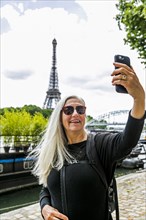 Caucasian woman posing for cell phone selfie near Eiffel Tower