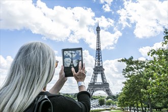 Caucasian woman photographing Eiffel Tower with digital tablet