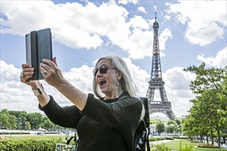 Caucasian woman posing for digital tablet selfie near Eiffel Tower