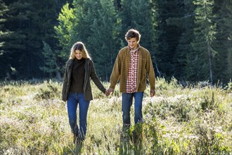 Caucasian couple walking in field holding hands