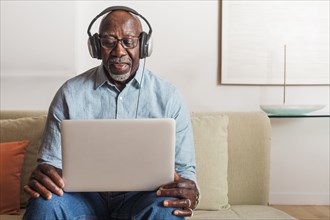 Man sitting on sofa listening to laptop with headphones
