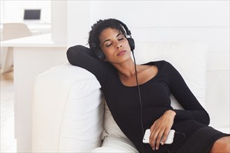 Mixed Race woman on sofa listening to cell phone with headphones