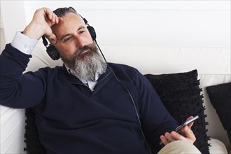 Pensive Caucasian man listening to cell phone with headphones