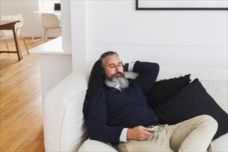 Caucasian man on sofa listening to cell phone with headphones